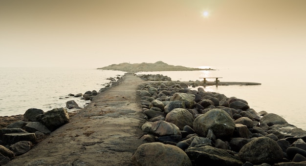 Muelle rodeado de piedras que atraviesan el mar tranquilo con el cielo soleado