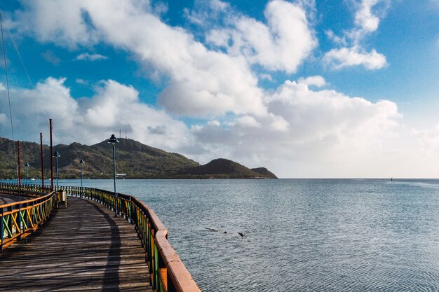 Muelle sobre el mar rodeado de montañas bajo un cielo nublado azul y la luz del sol