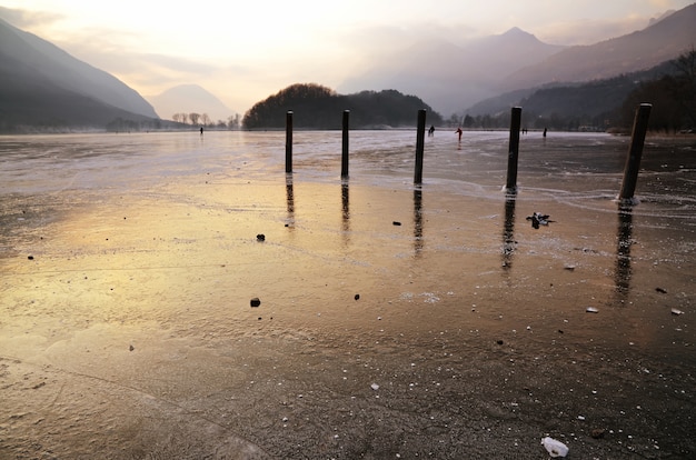 Muelles de madera en el lago helado y gente patinando sobre hielo.