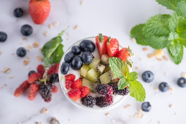 Muesli casero, tazón de granola de avena con yogur, arándanos frescos, moras, fresas, kiwi, menta y nueces para un desayuno saludable, copie el espacio. Concepto de desayuno saludable. Comer limpio.