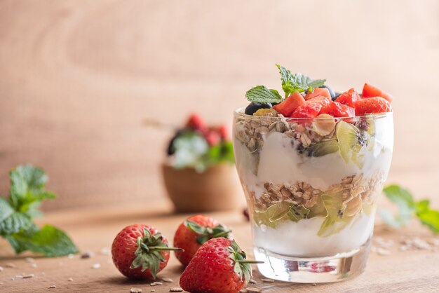 Muesli casero, tazón de granola de avena con yogur, arándanos frescos, moras, fresas, kiwi, menta y nueces para un desayuno saludable, copie el espacio. Concepto de desayuno saludable. Comer limpio.