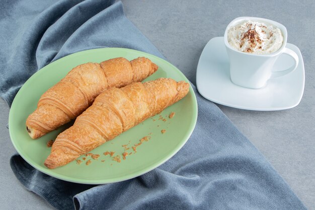 Una muestra de croissant en plato sobre toalla y con café, sobre el fondo de mármol. Foto de alta calidad