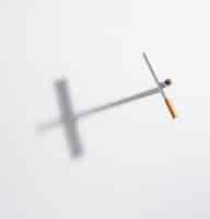 Foto gratuita la muestra de la cruz de la opinión de alto ángulo hecha de cigarrillo con ella sombra encendido aislado en el fondo blanco