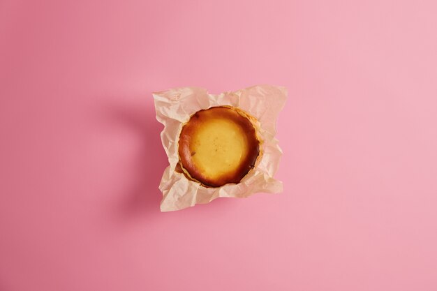 Muffin de queso casero embalado en paquete de papel aislado sobre fondo rosado. Confitería alta en calorías de panadería. Merienda dulce o comida de desayuno. Producto de panadería elaborado por chef gourmet.