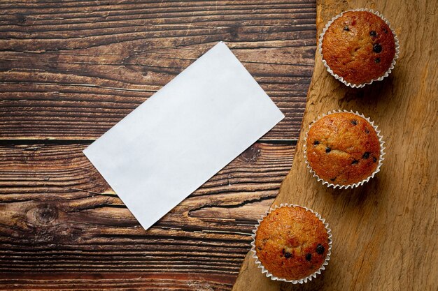 Muffins de chocolate y papel blanco vacío puesto sobre un piso de madera