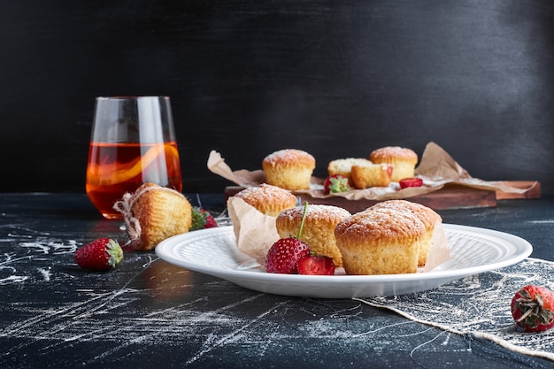 Muffins en un plato blanco con frutos rojos alrededor.