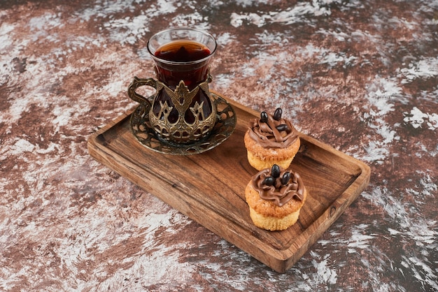 Muffins y un vaso de té en una tabla de madera.
