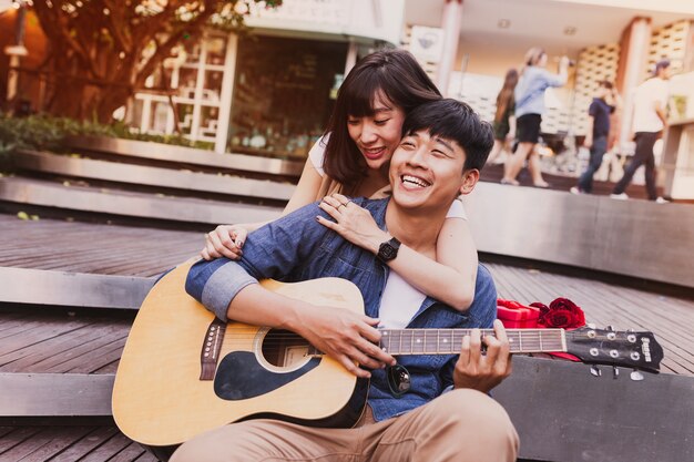 Mujer abrazando a un hombre mientras éste toca la guitarra