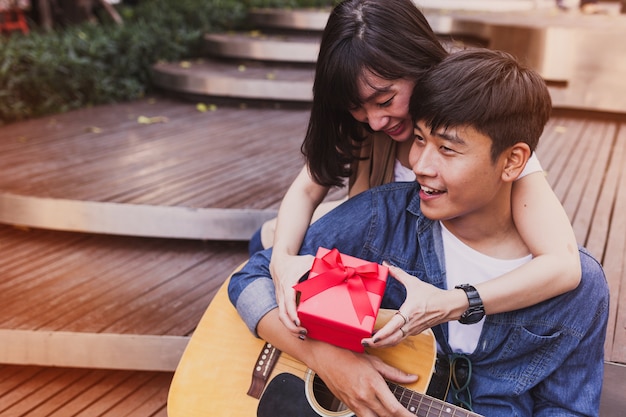 Foto gratuita mujer abrazando a un hombre y sosteniendo un regalo mientras éste toca la guitarra