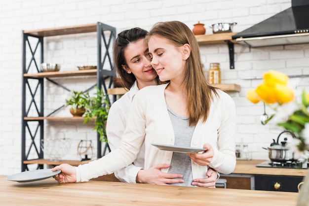 Foto gratuita mujer abrazando a su novia por detrás arreglando las placas de cerámica en la mesa