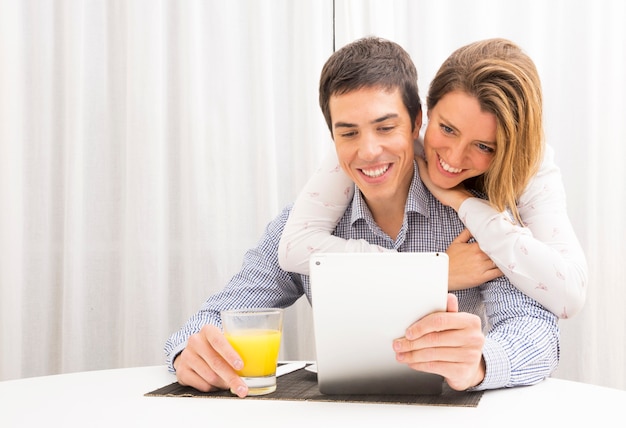 Mujer abrazando a su novio por detrás mirando la tableta digital con jugo