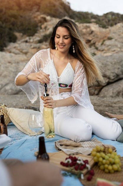 Mujer abriendo una botella de vino en la playa