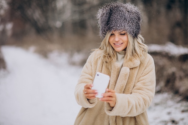 Mujer en abrigo de invierno caminando en el parque lleno de nieve hablando por teléfono