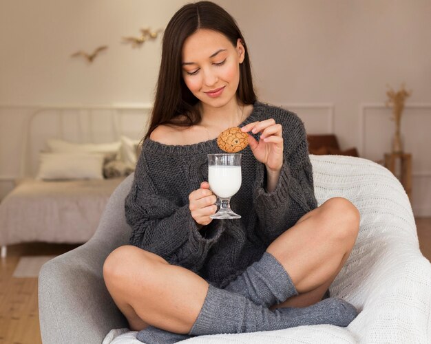 Mujer acogedora en sillón con galleta y leche