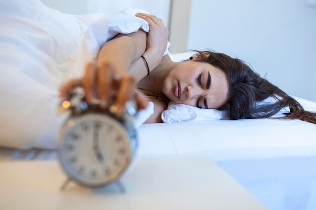 Mujer acostada en la cama apagando un despertador por la mañana a las 5 a.m. La mano apaga el despertador despertándose a la mañana niña apaga el despertador despertándose por la mañana de una llamada