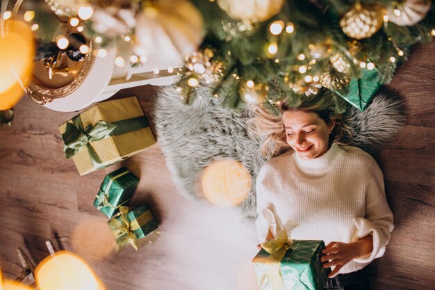 Mujer acostada debajo del árbol de Navidad con regalos