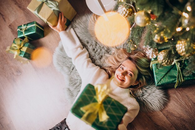 Mujer acostada debajo del árbol de Navidad con regalos