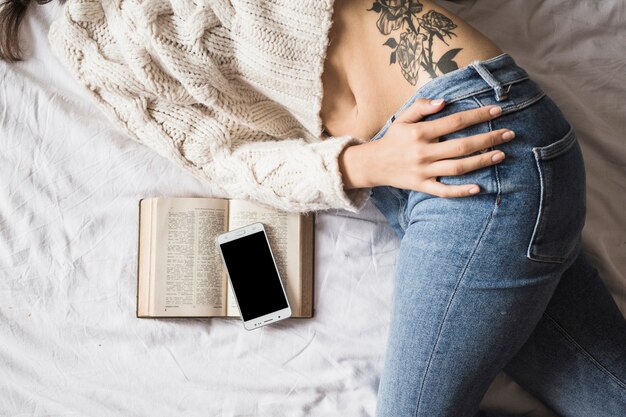 Mujer acostada en sábana con smartphone y libro