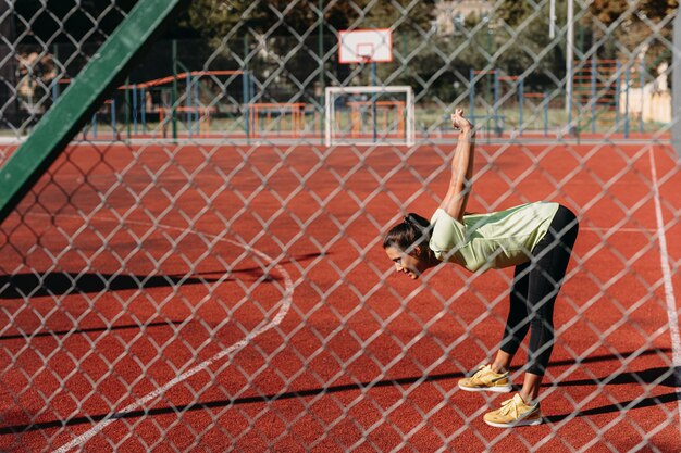 Mujer activa en ropa deportiva estirando el cuerpo al aire libre