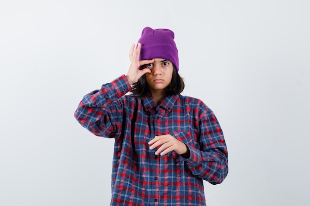 Foto gratuita mujer adolescente abriendo el ojo con los dedos en camisa a cuadros y gorro