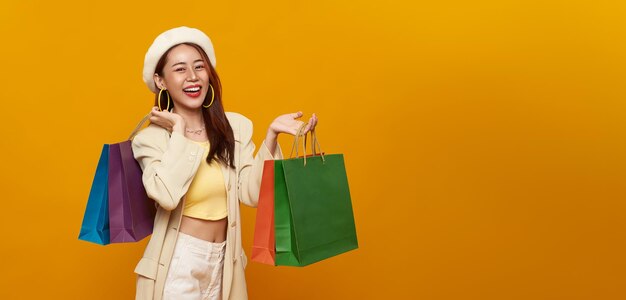 Mujer adolescente asiática sonriente que lleva bolsas de compras en el fondo del estudio de color amarillo