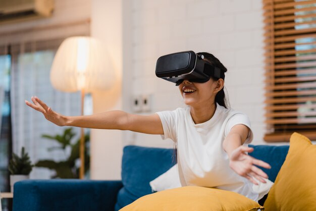 Mujer adolescente asiática usando gafas simulador de realidad virtual jugando videojuegos en la sala de estar