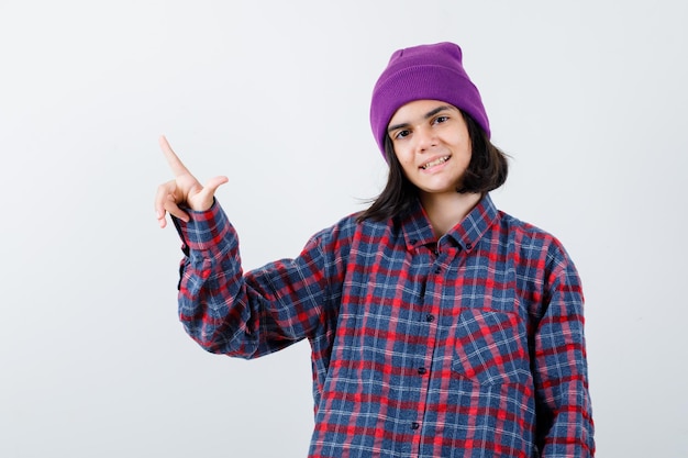 Mujer adolescente en camisa a cuadros y gorro gesticulando aislado