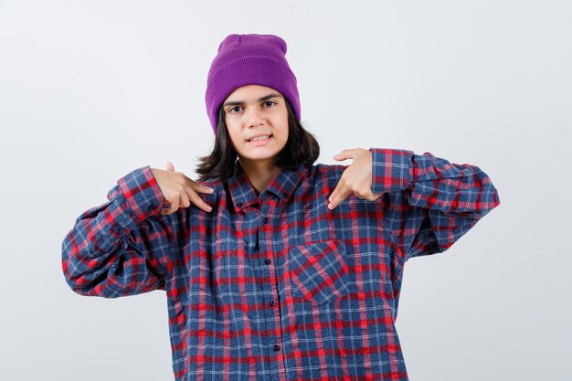 Mujer adolescente en camisa a cuadros y gorro gesticulando aislado