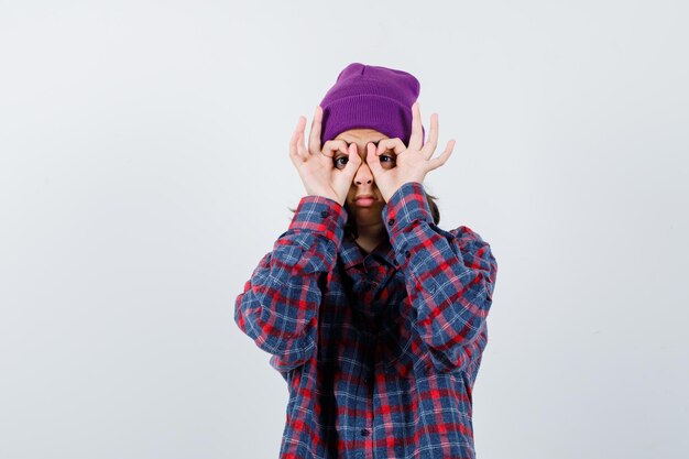 Mujer adolescente en camisa a cuadros gorro morado mostrando gafas gesto mirando lindo