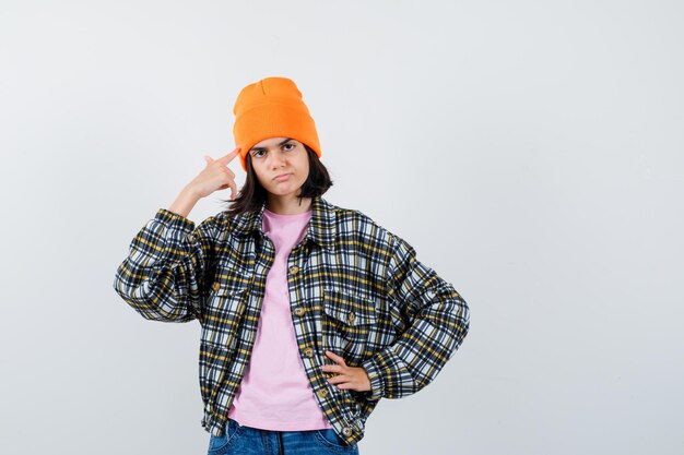 Mujer adolescente en camiseta chaqueta beanie sosteniendo el dedo en las sienes mirando serio