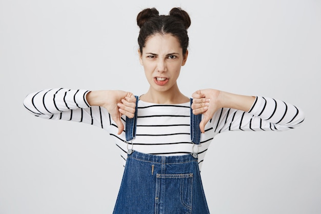 Foto gratuita mujer adolescente decepcionada con los pulgares hacia abajo y haciendo muecas