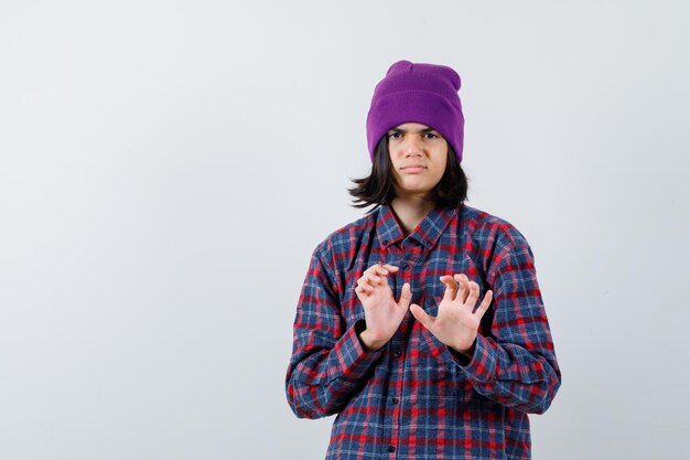 Mujer adolescente manteniendo las manos para defenderse en camisa a cuadros y gorro