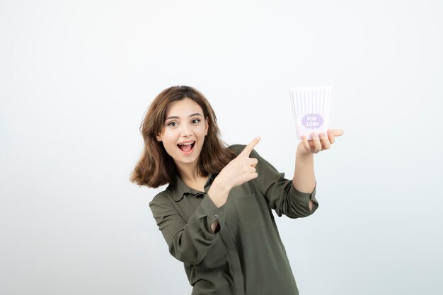 Mujer adorable joven apuntando a la caja de palomitas de maíz y posando. foto de alta calidad