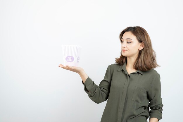 Mujer adorable joven que mira la caja de palomitas de maíz sobre blanco. foto de alta calidad