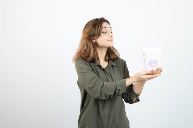 Mujer adorable joven que mira la caja de palomitas de maíz sobre blanco. foto de alta calidad