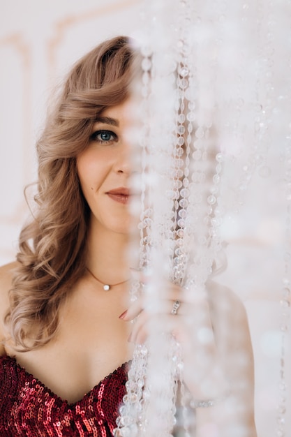 Foto gratuita la mujer adorable en el vestido rojo de borgoña presenta en un cuarto de lujo brillante con la lámpara grande