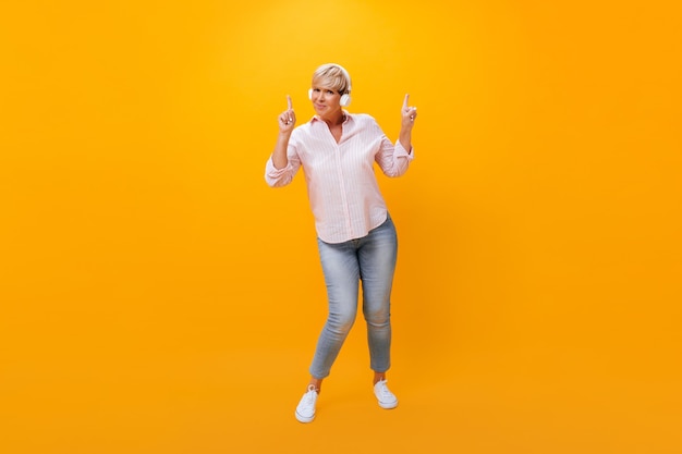 Mujer adulta en auriculares apuntando hacia arriba sobre fondo naranja