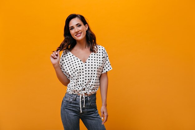 Mujer adulta en blusa y jeans posando sobre fondo naranja