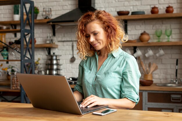 Mujer adulta con una computadora portátil en la cocina