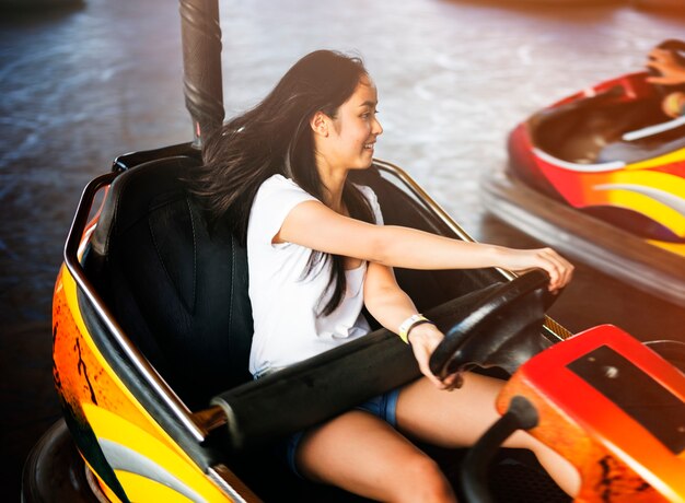 Mujer adulta joven que juega en el coche de parachoques en el parque de atracciones