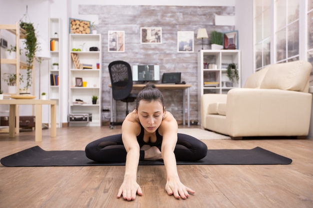 Mujer adulta con los ojos cerrados sentada en postura de yoga de loto relajando la espalda y estirando hacia adelante.