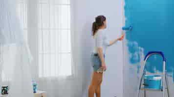 Foto gratuita mujer adulta pintando la pared con un cepillo de rodillo bañado en pintura azul. diseñador de viviendas renovar, renovar. redecoración de apartamentos y construcción de viviendas mientras se renueva y mejora. reparación y decoración