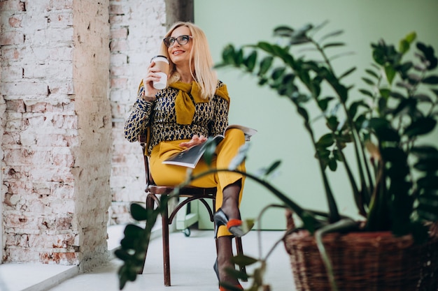 Mujer adulta sentada en una silla tomando café y leyendo una revista