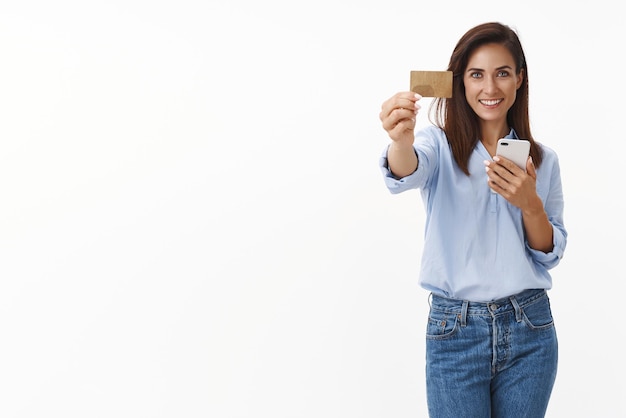 Una mujer adulta sincera y agradable recomienda la banca móvil, sostenga un teléfono inteligente, muestre la tarjeta de crédito y sonría una buena oferta satisfecha Esposa que compra boletos de avión de reserva en línea