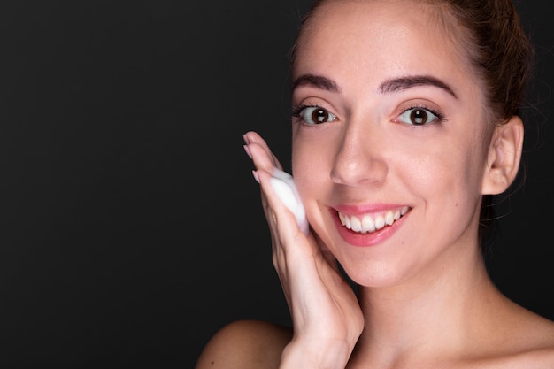Mujer adulta sonriente tratando producto de cuidado de la piel