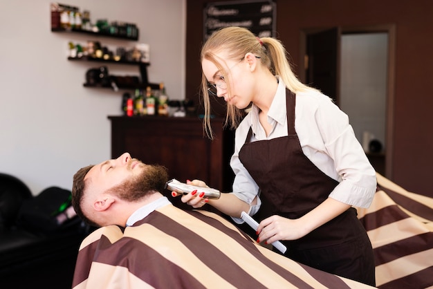 Mujer afeitándose el bigote de su cliente en la peluquería