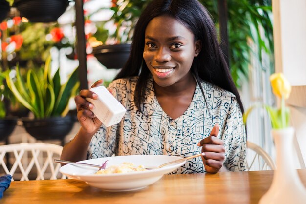 Mujer africana agregando sal a la comida en el restaurante.
