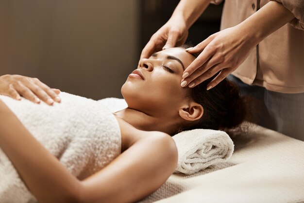 Mujer africana atractiva que disfruta de masaje facial en salón del balneario.