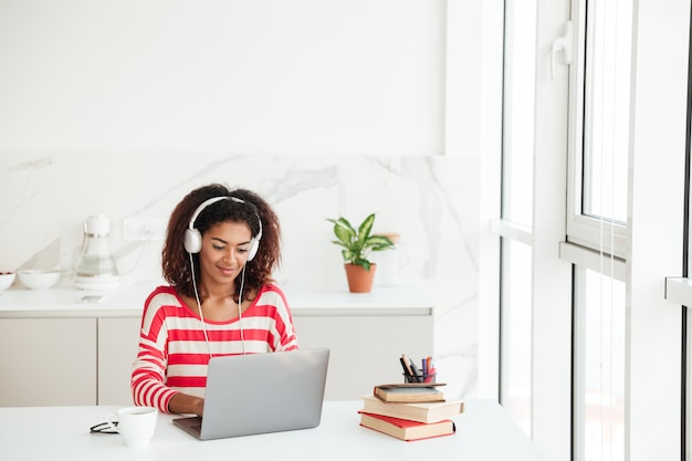 Mujer africana atractiva sonriente que usa la computadora portátil