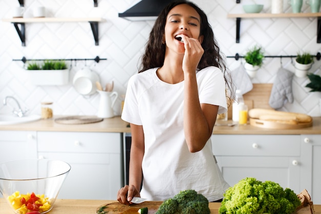 Mujer africana bastante joven que cocina comiendo un pepino